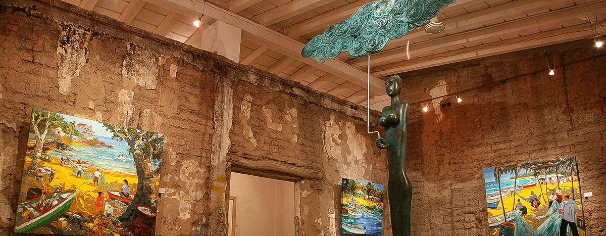 Interior de galería de arte con pinturas y una escultura de una mujer bajo una estructura en forma de nube